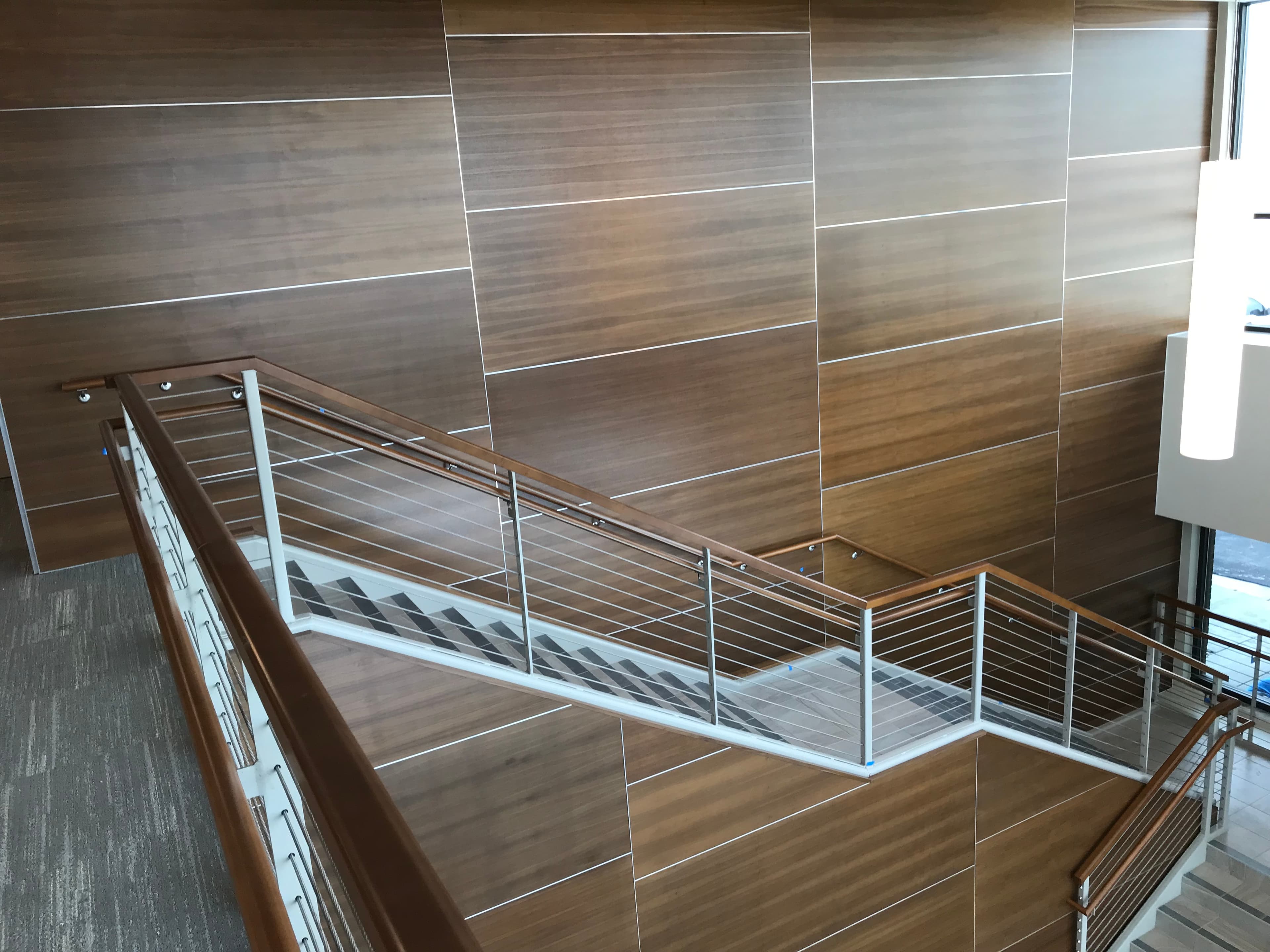 Walnut veneer wall panels with metal reveals beside a wood-capped cable-rail staircase