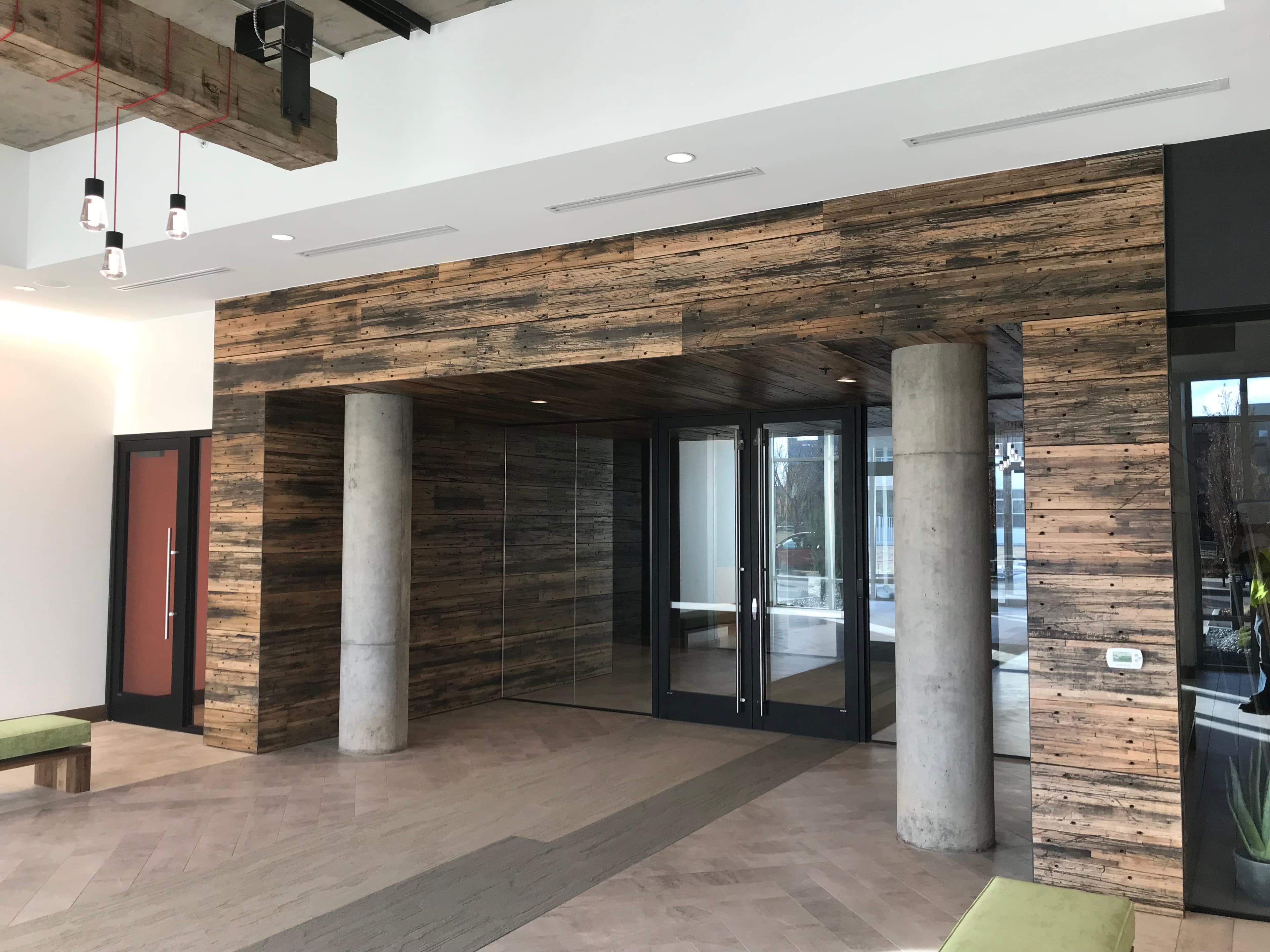 Reclaimed wood cladding framing glass entry doors between two concrete columns